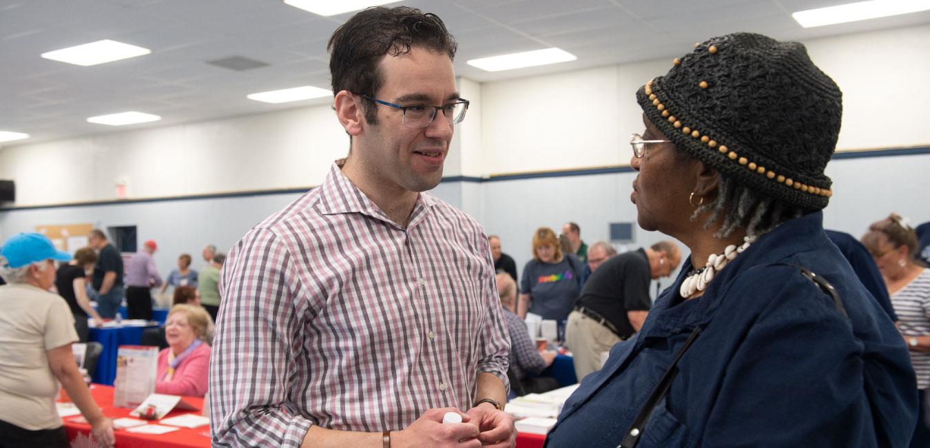 Representative Schlossberg speaking to elderly woman wearing hat at indoor event