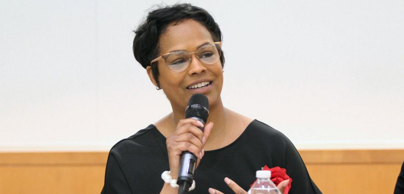 Representative Cephas wearing red rose, holding microphone and speaking