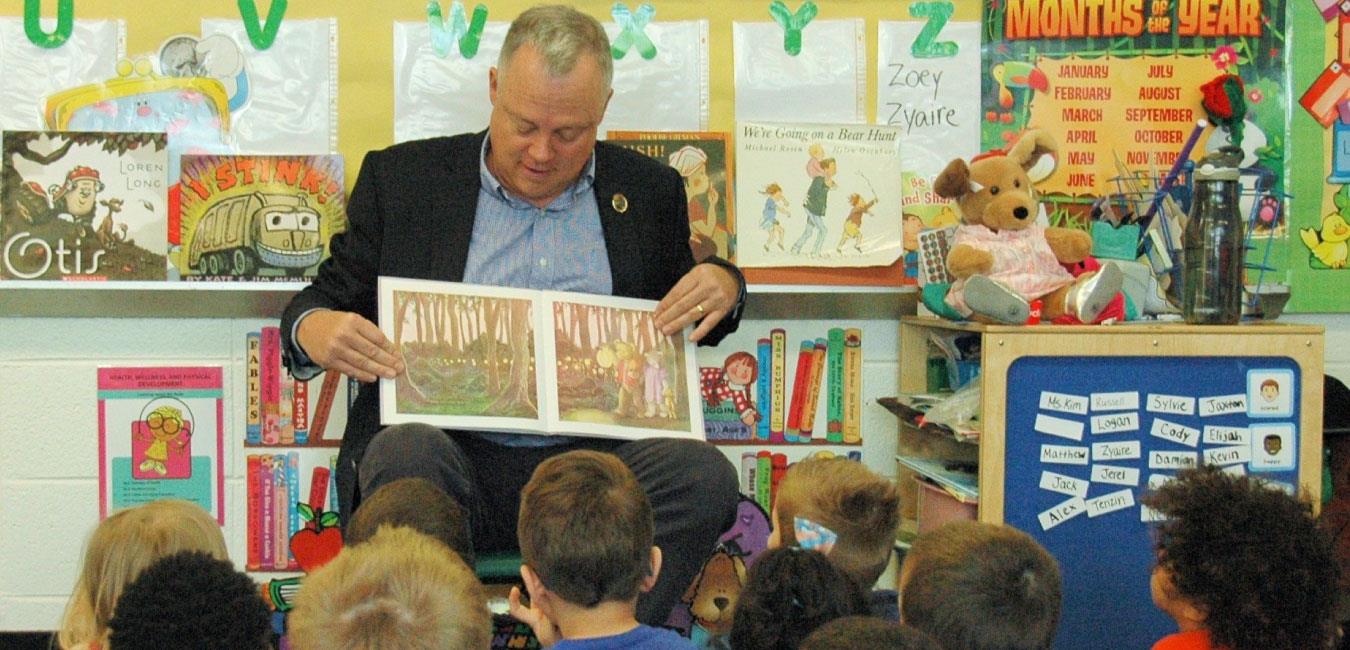 Representative Warren reading to group of young students sitting on floor in classroom