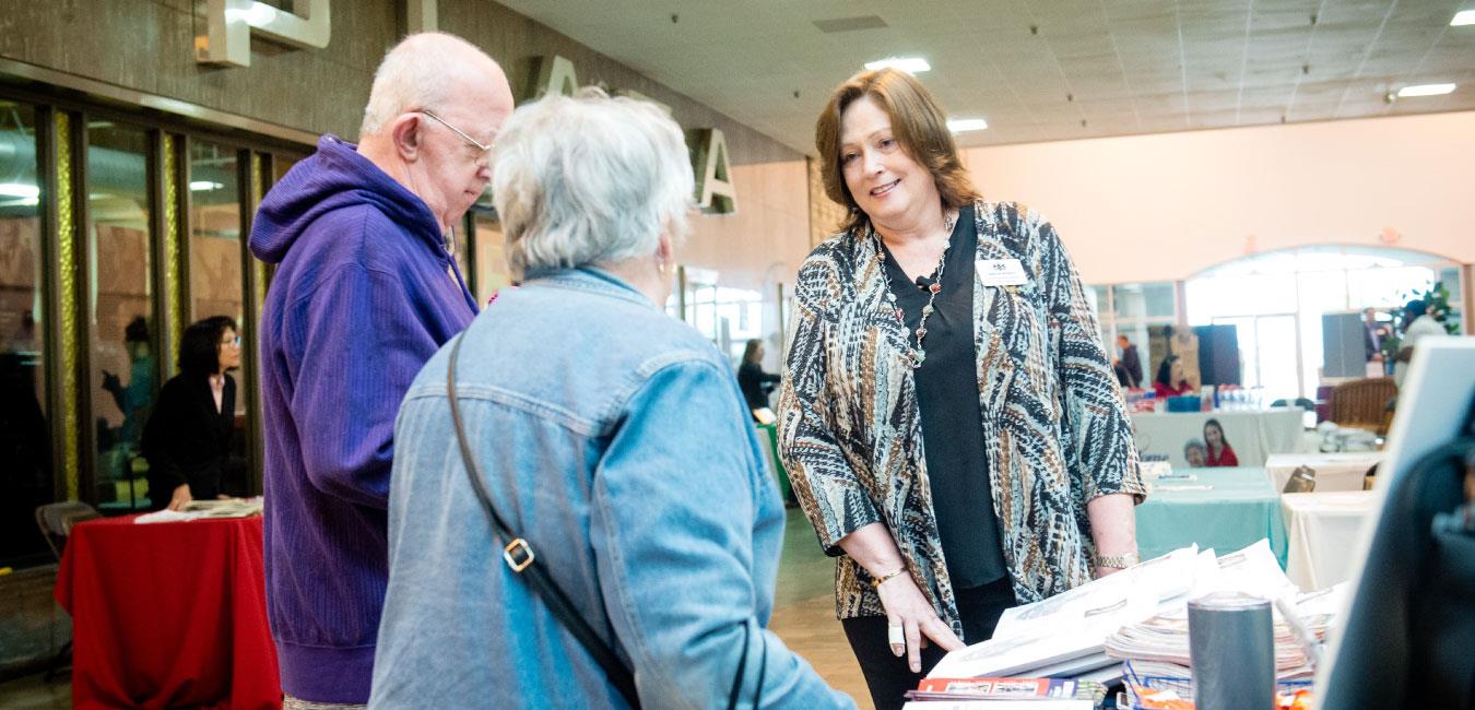 Representative McNeill speaking to elderly couple at indoor event