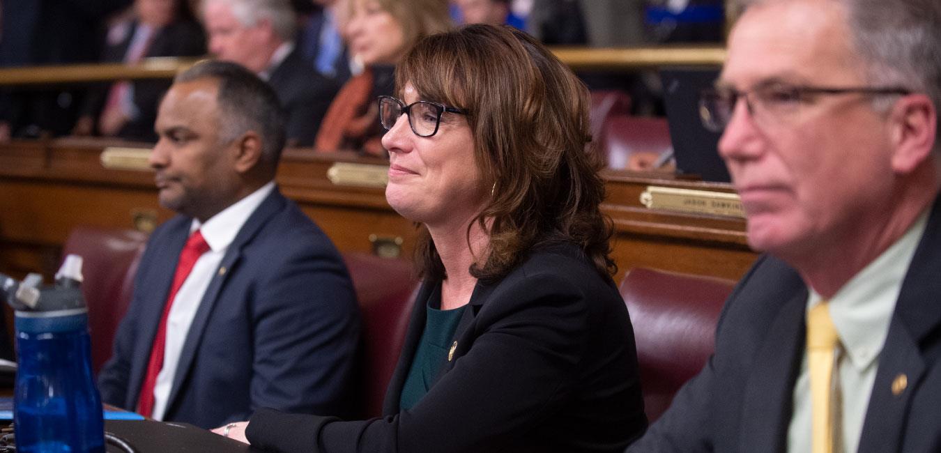 Representative Isaacson looking onward and listening while sitting in her seat on the House floor