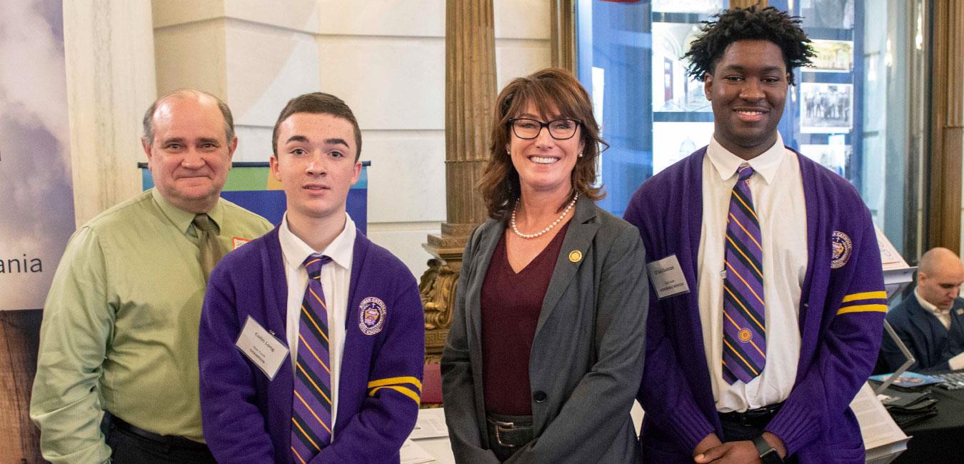 Representative Isaacson posing for photo with students dressed in matching uniforms