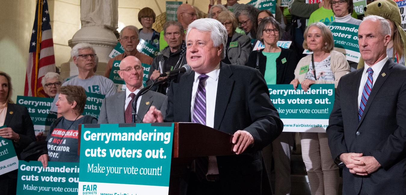 Representative Samuelson speaking at podium in front of group rallying to end gerrymandering on Capitol rotunda steps