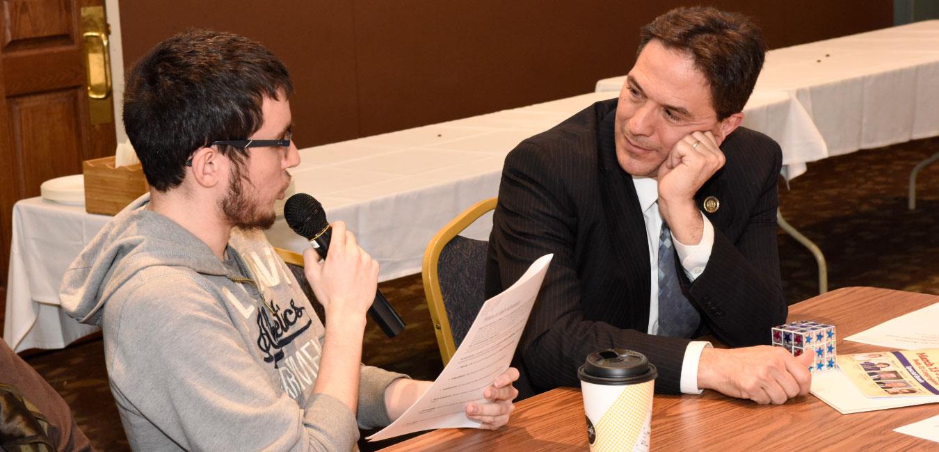 Representative Hohenstein sitting and listening to young man speaking into microphone