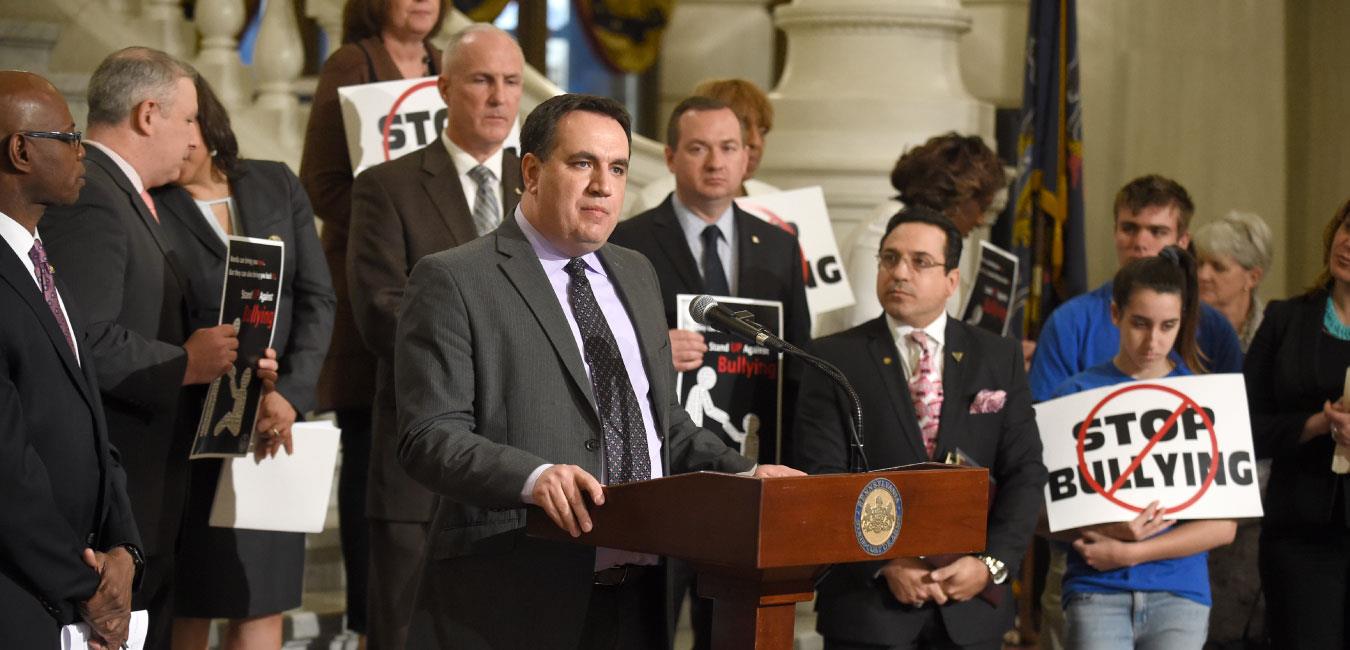 Representative Burns speaking at podium on Capitol steps with fellow legislators at anti-bullying event