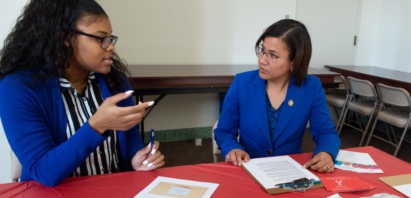 Representative Bullock speaking to woman sitting at table with clip board