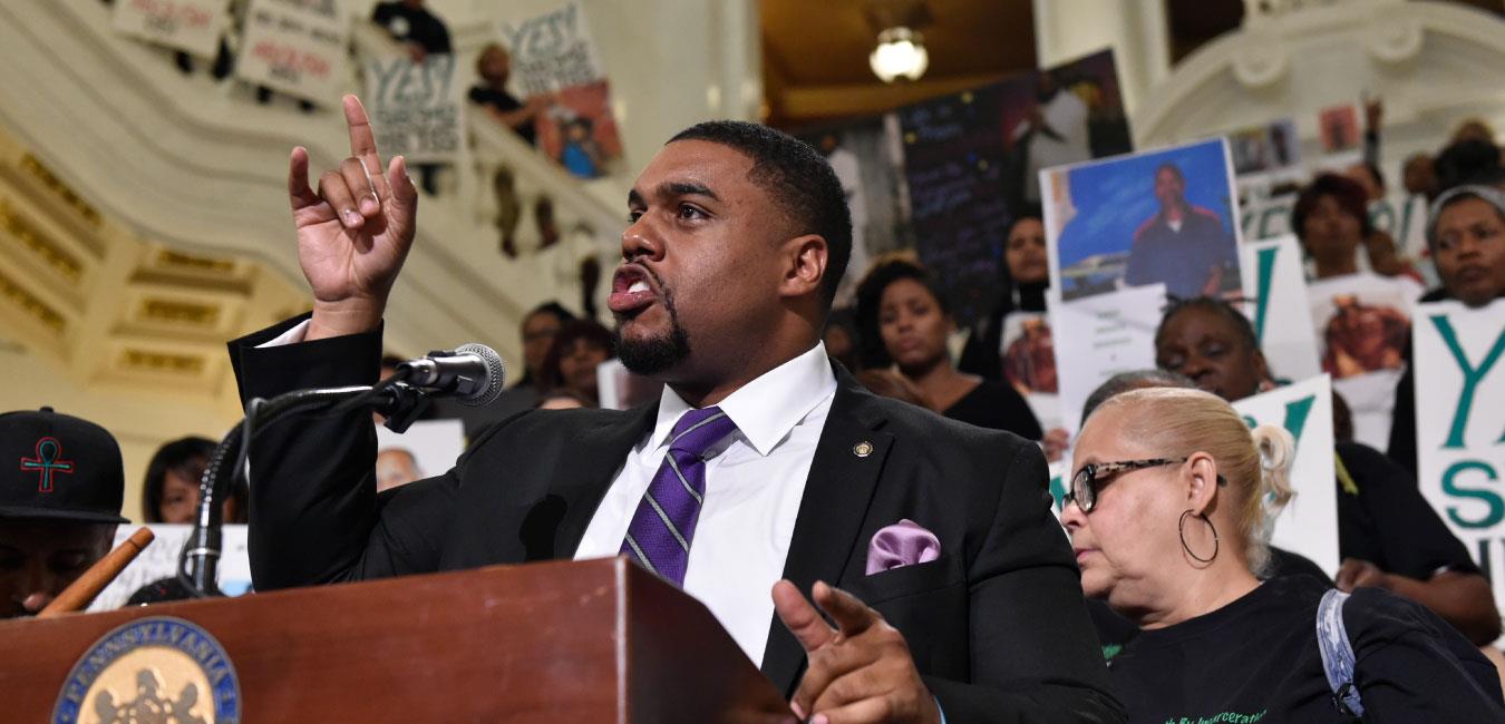 Representative Dawkins pointing upward and speaking at podium in front of activists on Capitol rotunda steps