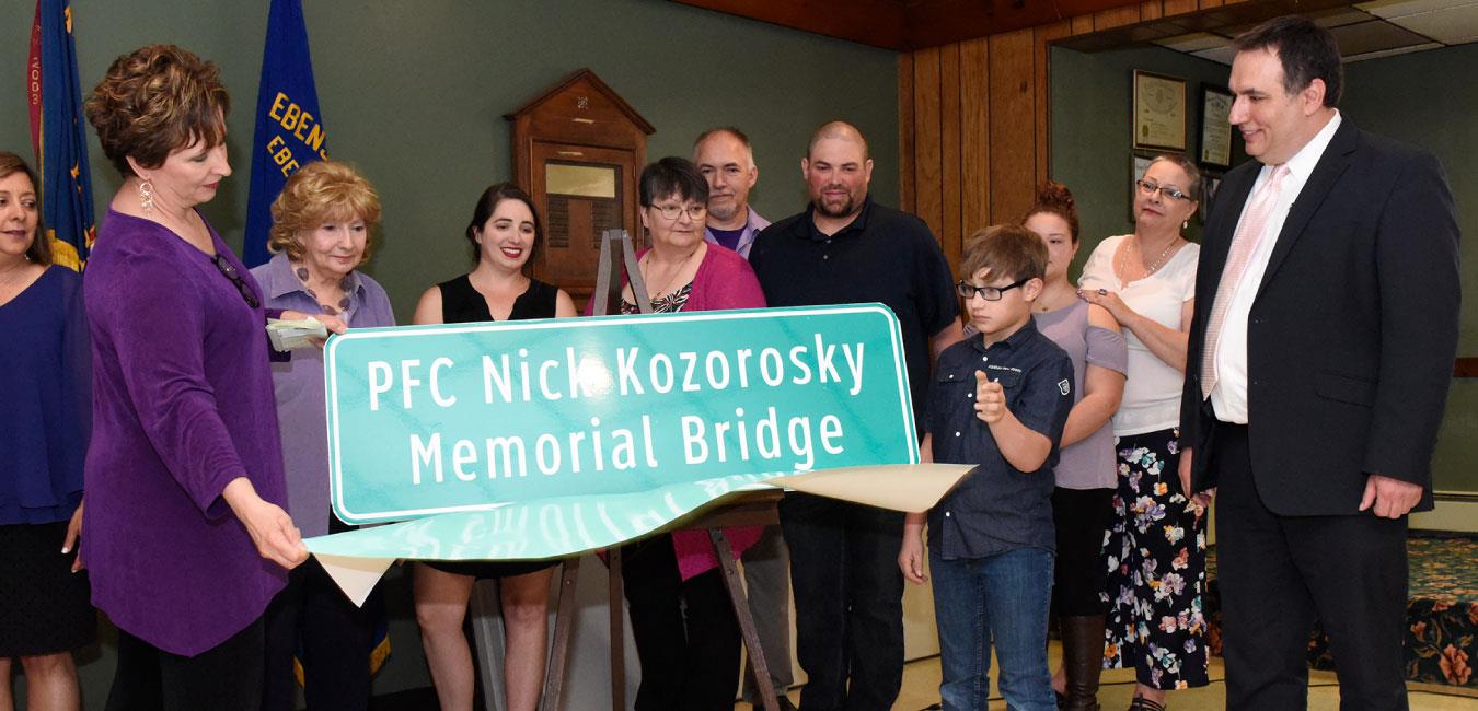 Representative Burns standing with group at unveiling of sign for PFC Nick Kozorosky Memorial Bridge