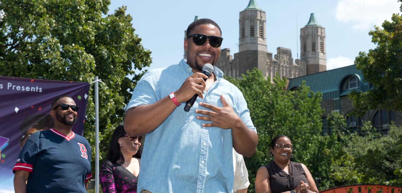 Representative Dawkins wearing sunglasses, smiling, holding microphone and speaking to group of people