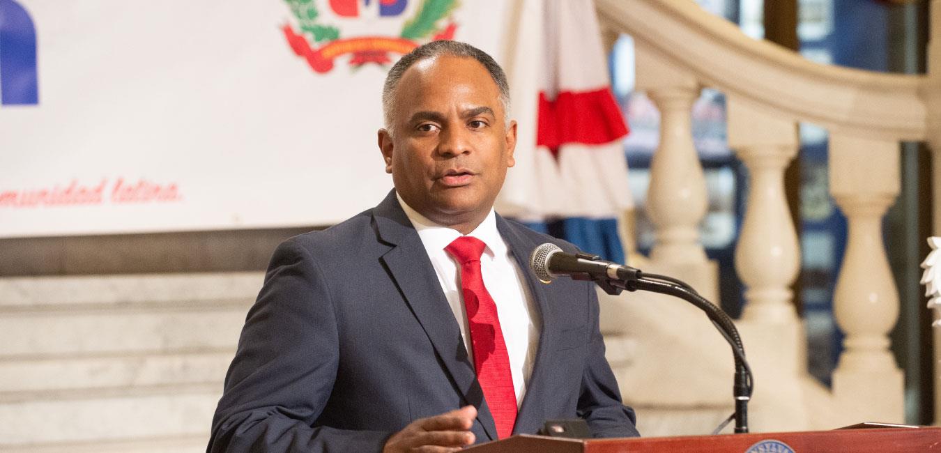 Representative Burgos speaking at podium in front of Capitol rotunda steps