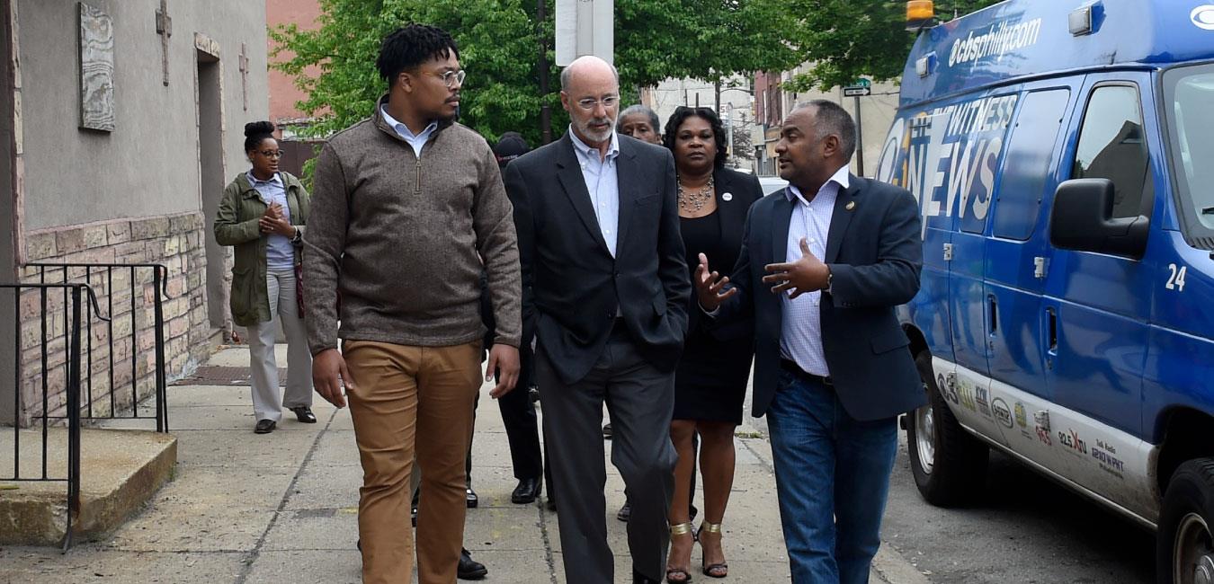 Representative Burgos walking on sidewalk and talking with group including Governor Wolf and Representative Kenyatta