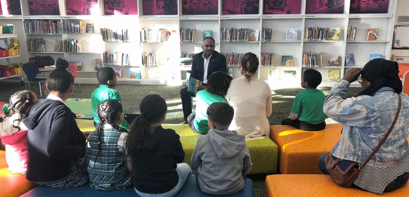 Representative Burgos sitting and reading to group of students in library