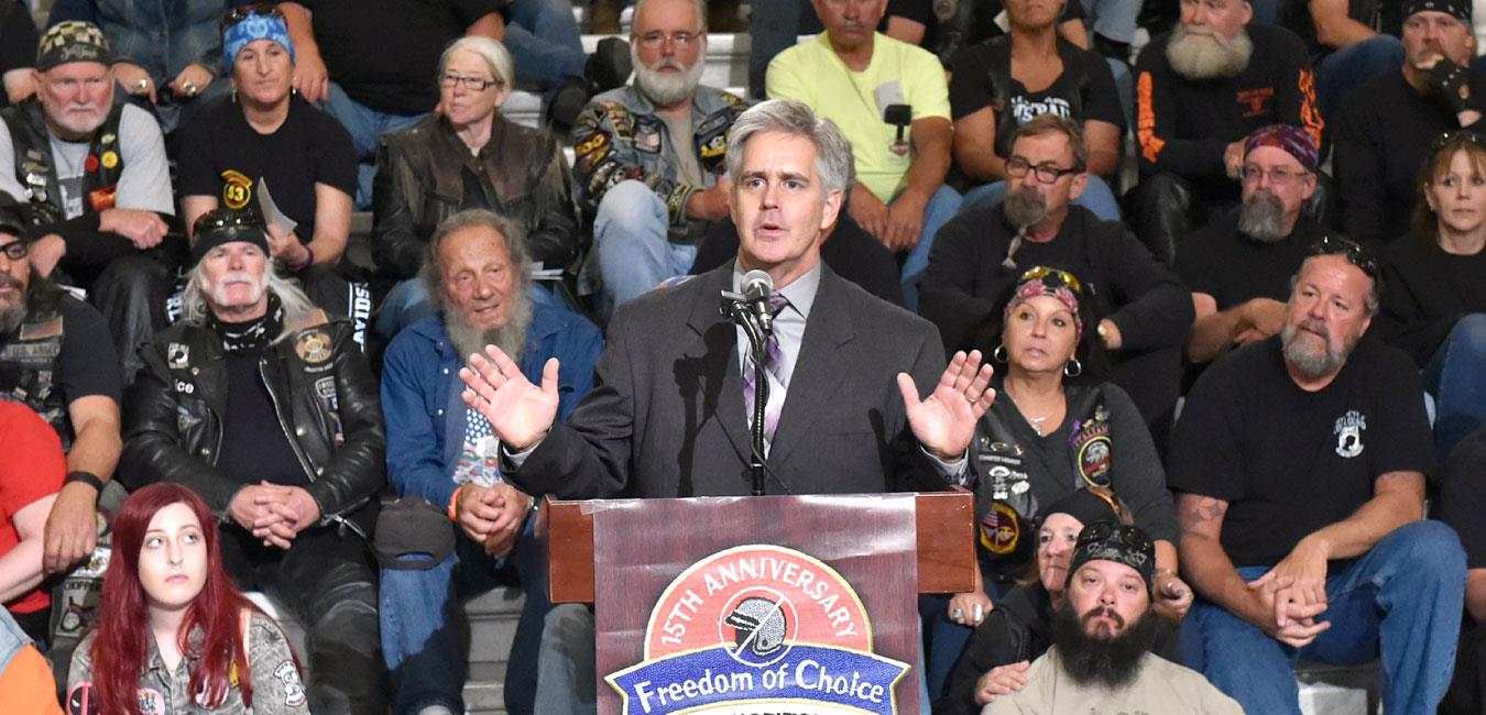 Representative Conklin speaking at podium in front of motorcycle activist group