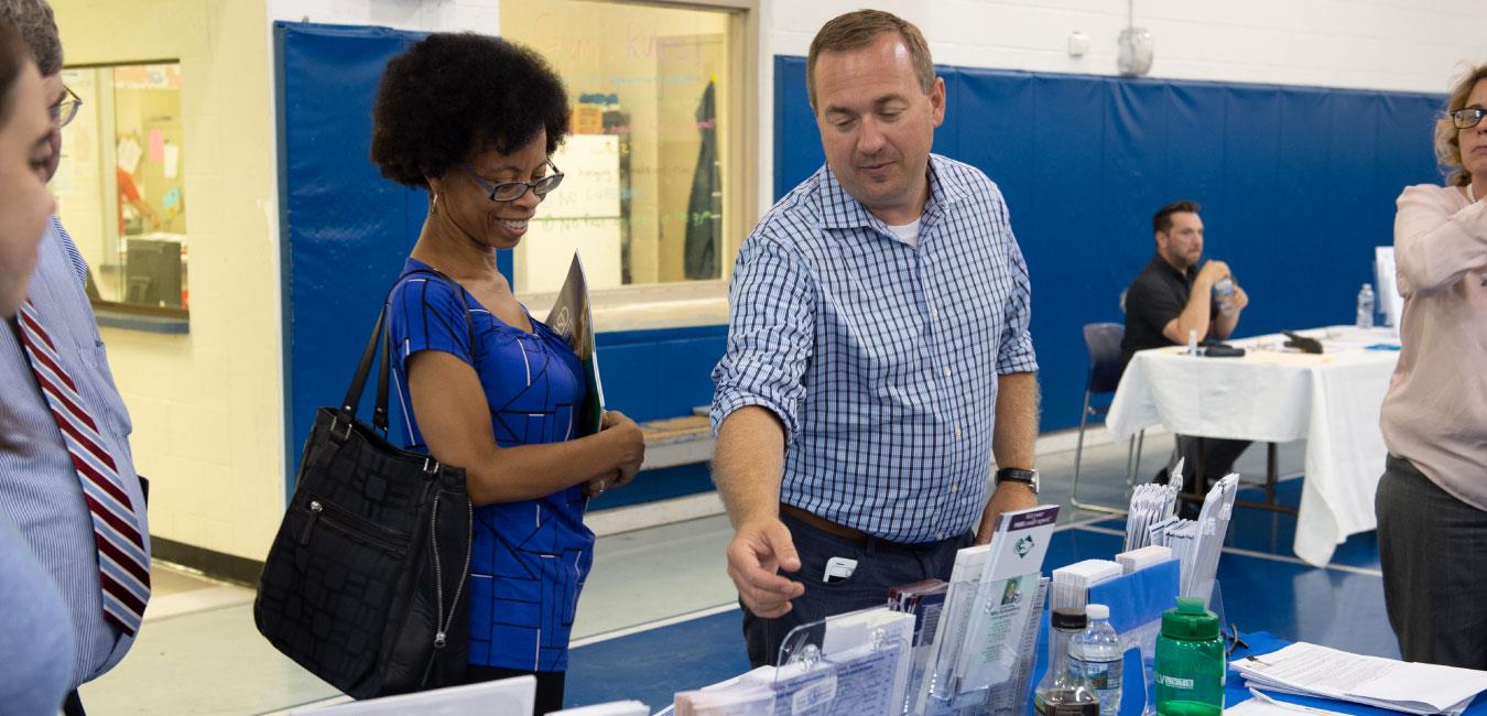 Representative Schweyer reaching for leaflet and speaking to smiling woman at indoor event