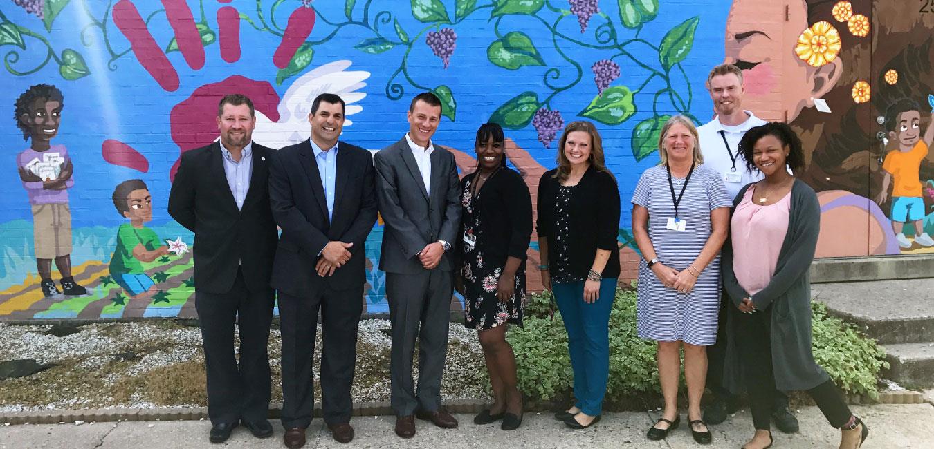 Representative Rozzi posing for photo with group of people standing in front of building mural