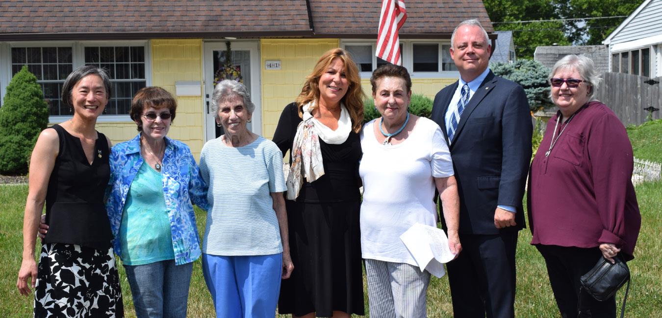 Representative Tina Davis posing for photo with group of people outside of yellow house