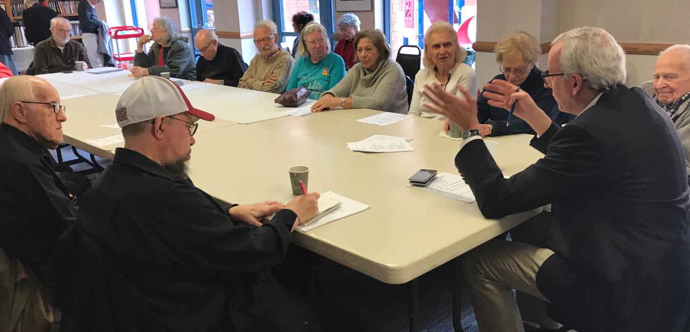 Representative Frankel sitting at table speaking to group of senior citizens