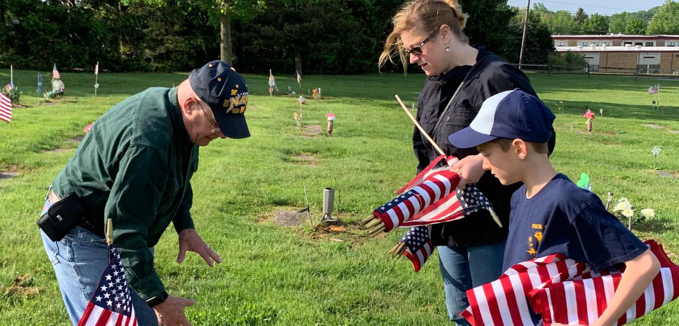 Representative Krueger with older man and young boy putting American flags on graves in cemetery