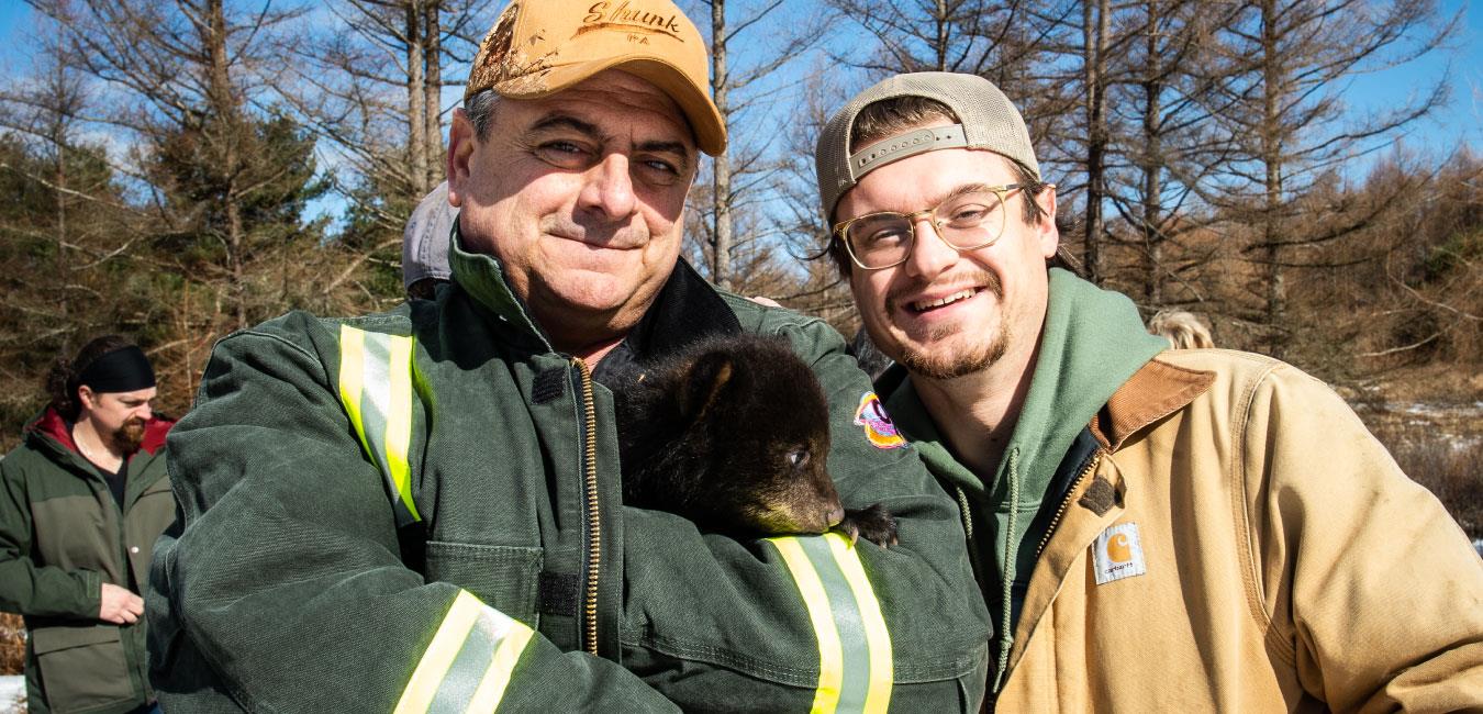 Representative Delloso holding baby bear in green jacket and posing for photo with man