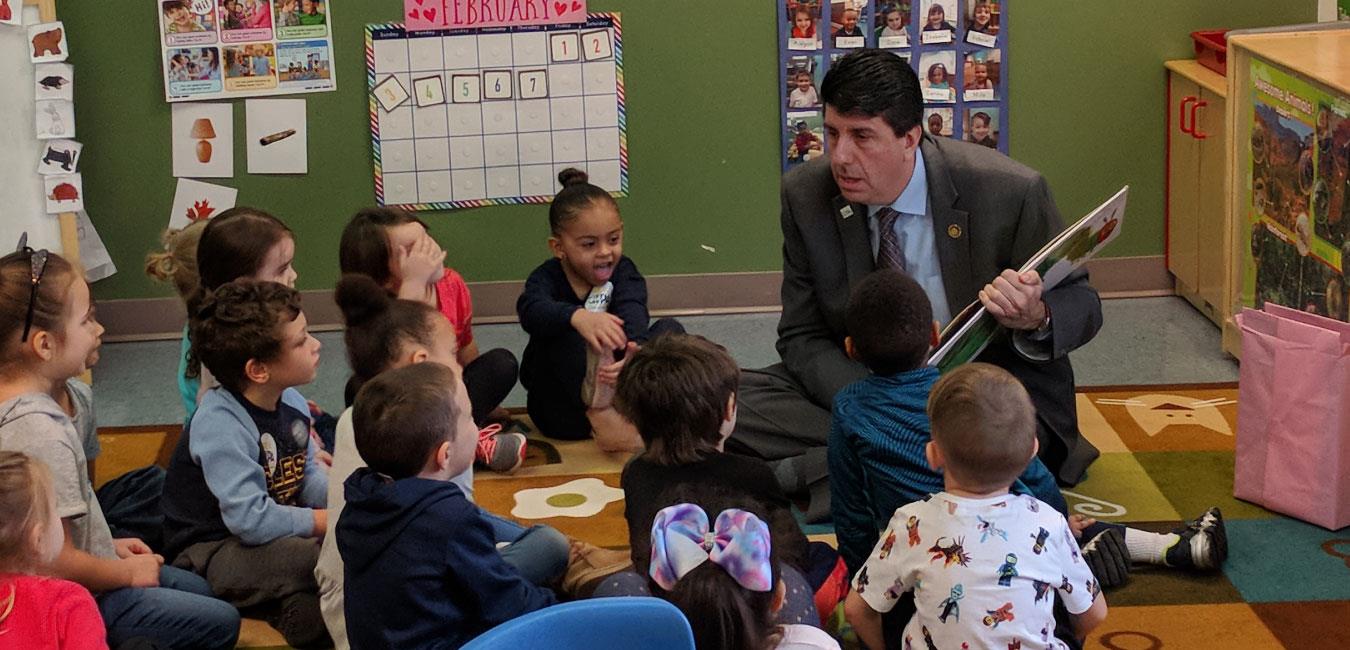 Representative Ciresi sitting on floor and reading The Very Hungry Caterpillar to group of young students