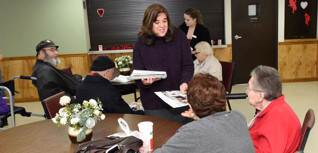 Representative Kulik smiling and handing out fliers to seniors sitting at table