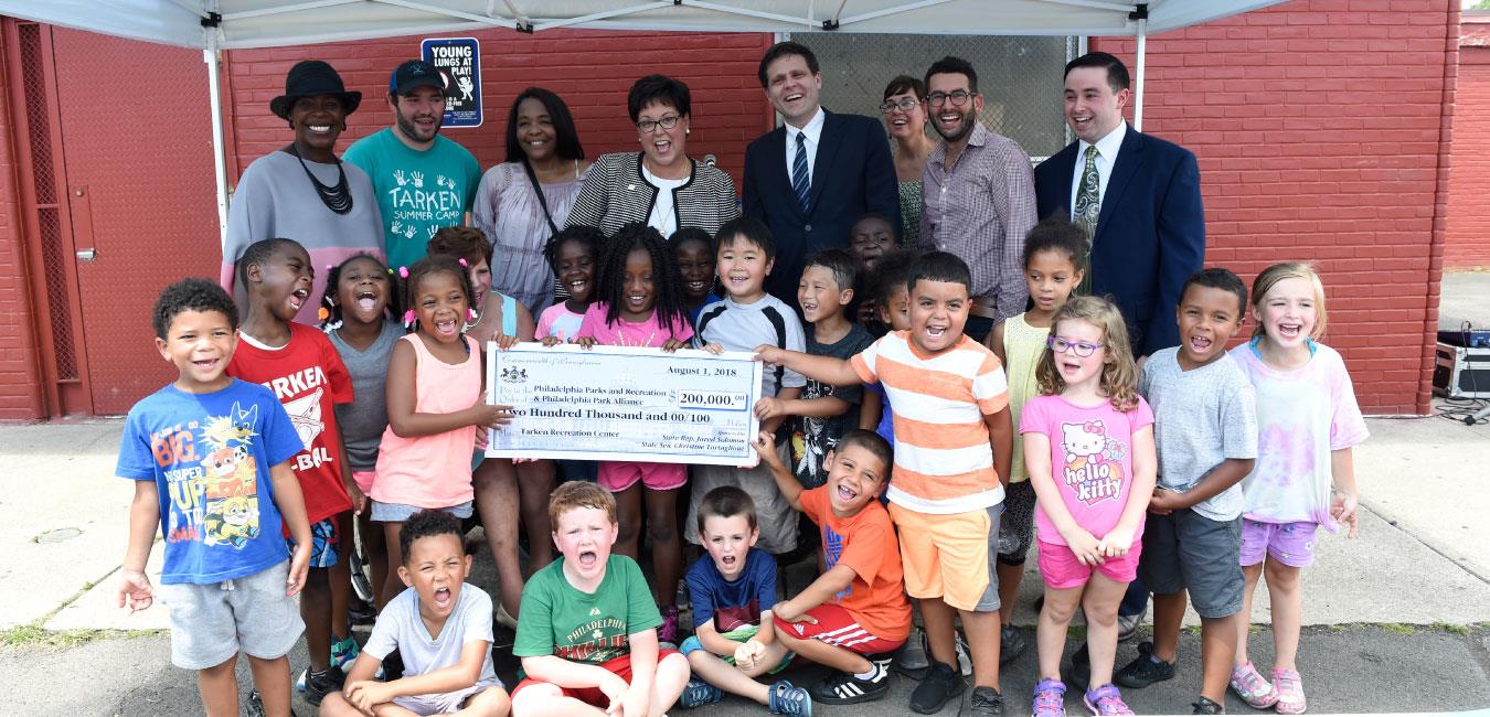 Representative Solomon posing for photo with children holding big check for Philadelphia Parks and Recreation