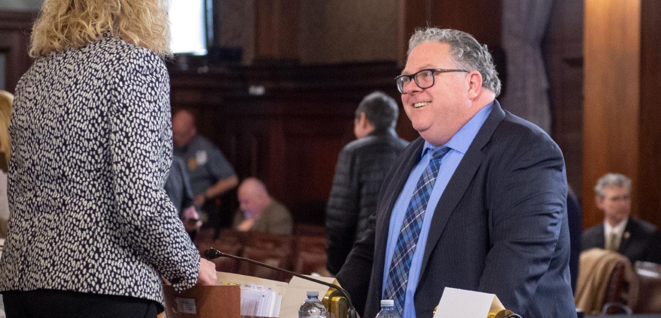 Representative Briggs smiling and speaking to member of legislative staff on House floor