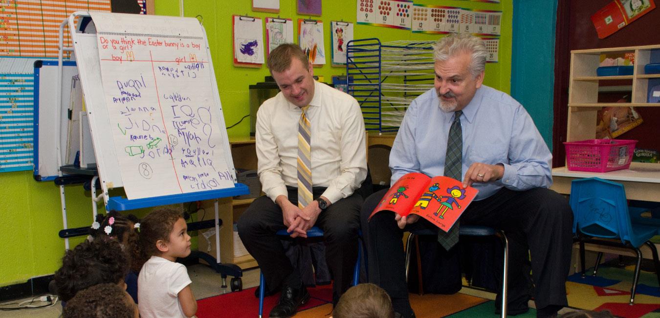 Representative Sturla pointing to page reading book to class of young students