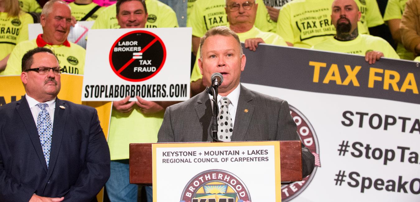 Representative Harkins speaking at podium in front of Brotherhood of Carpenters members on Capitol rotunda steps