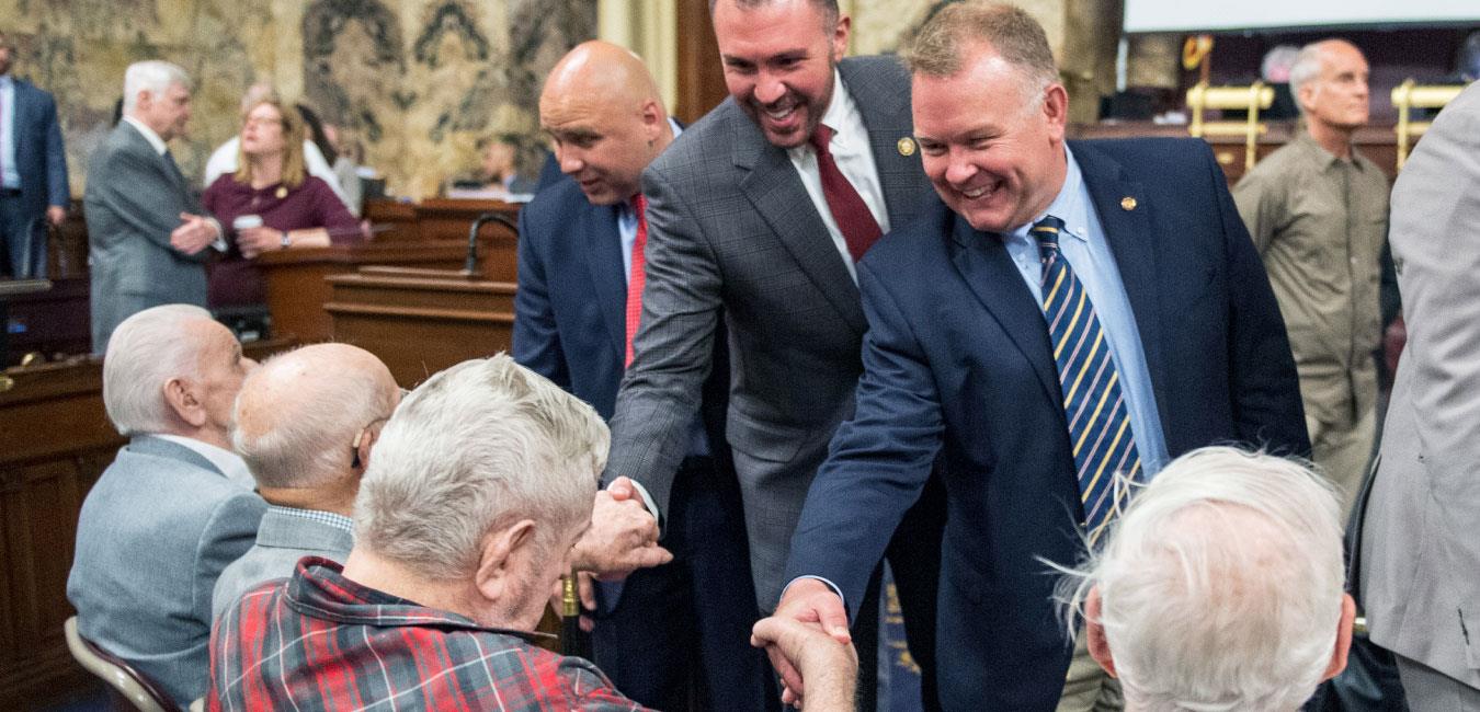 Representative Harkins smiling and shaking hands with elderly men on House floor