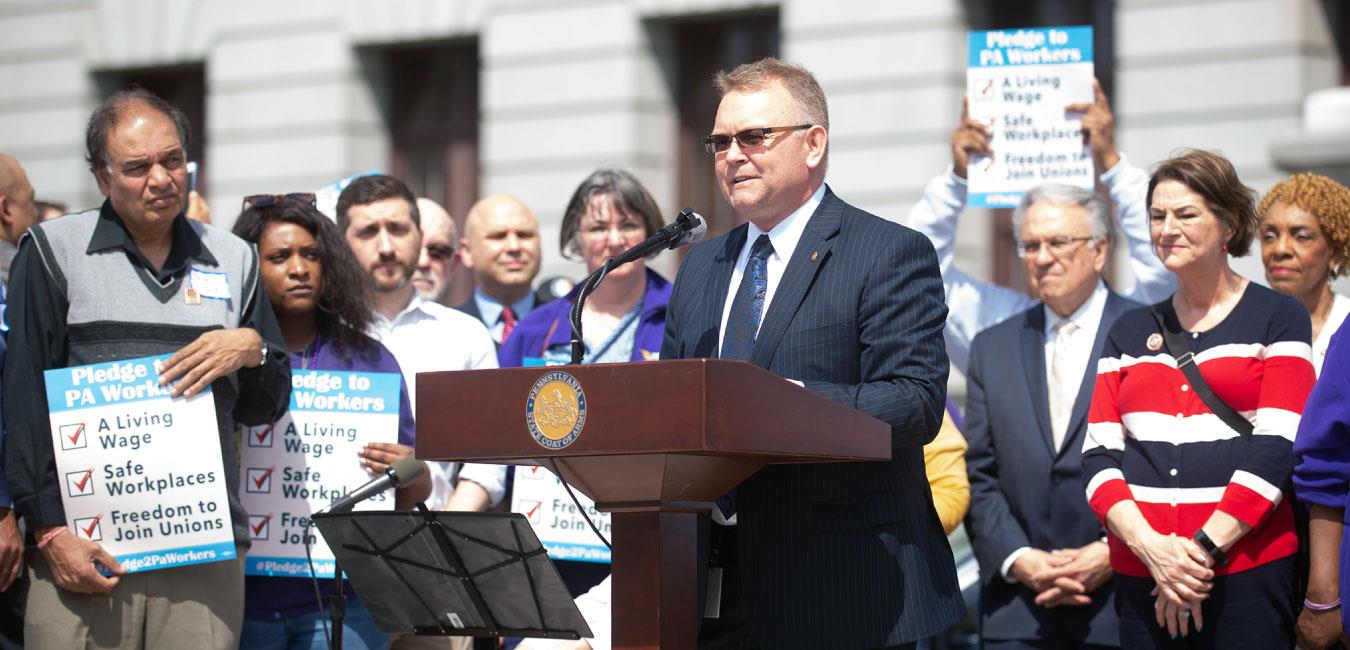 Representative Harkins speaking at podium in front of minimum wage activists in front of Capitol