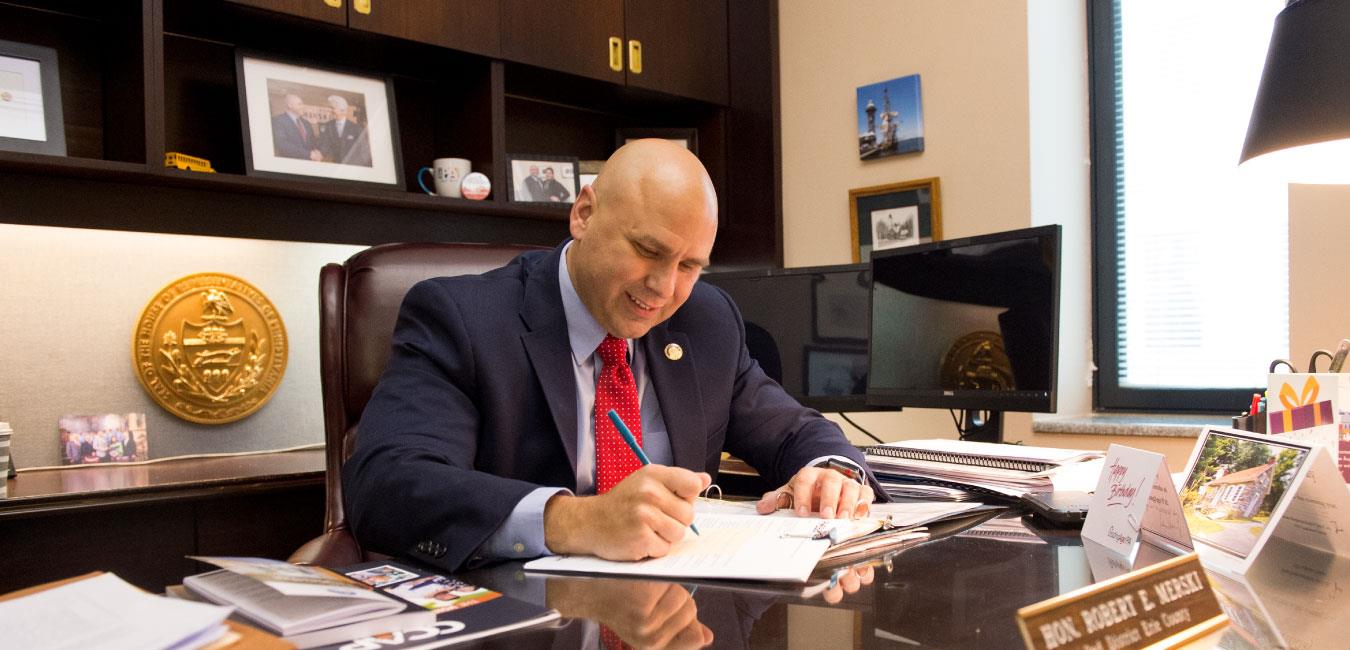 Representative Merski writing on paper at desk in his office