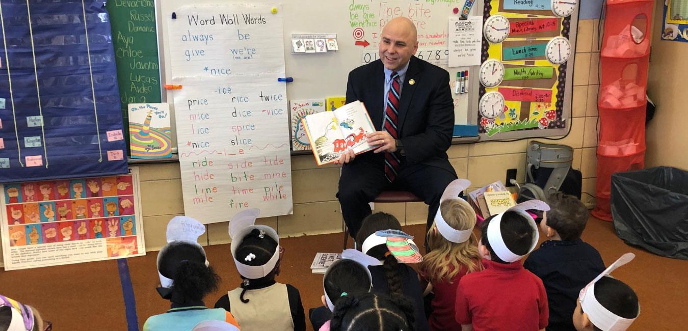 Representative Merski reading Dr. Seuss book to group of students sitting on floor