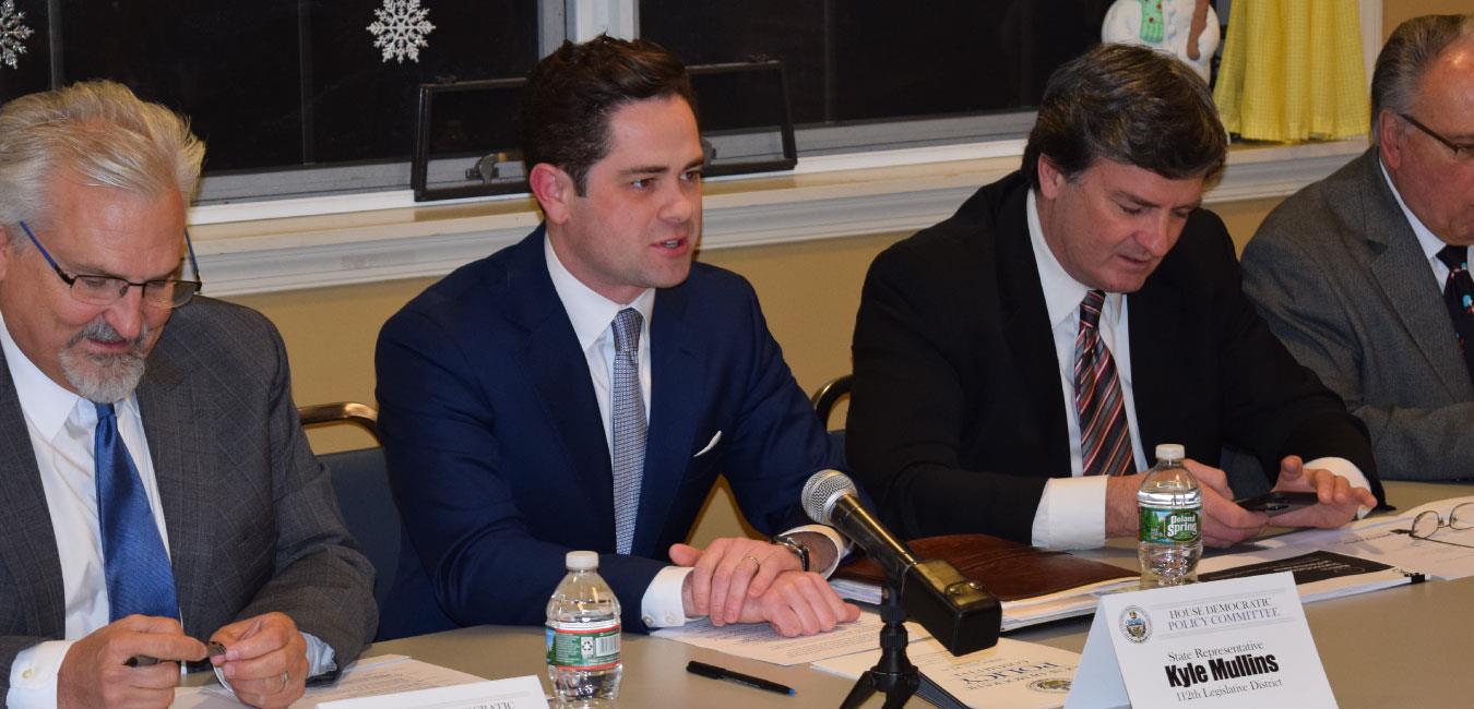 Representative Mullins speaking into microphone next to fellow lawmakers at hearing