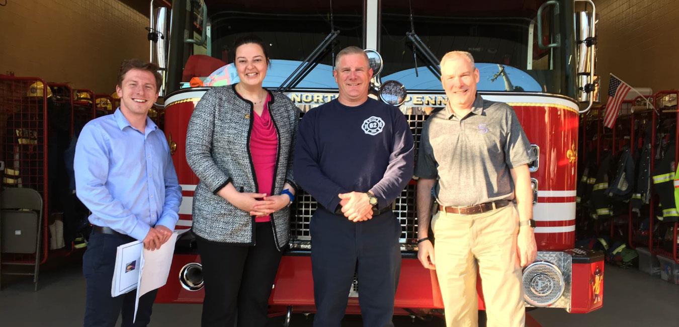 Representative Hanbidge posing for photo with firefighters in front of firetruck in station