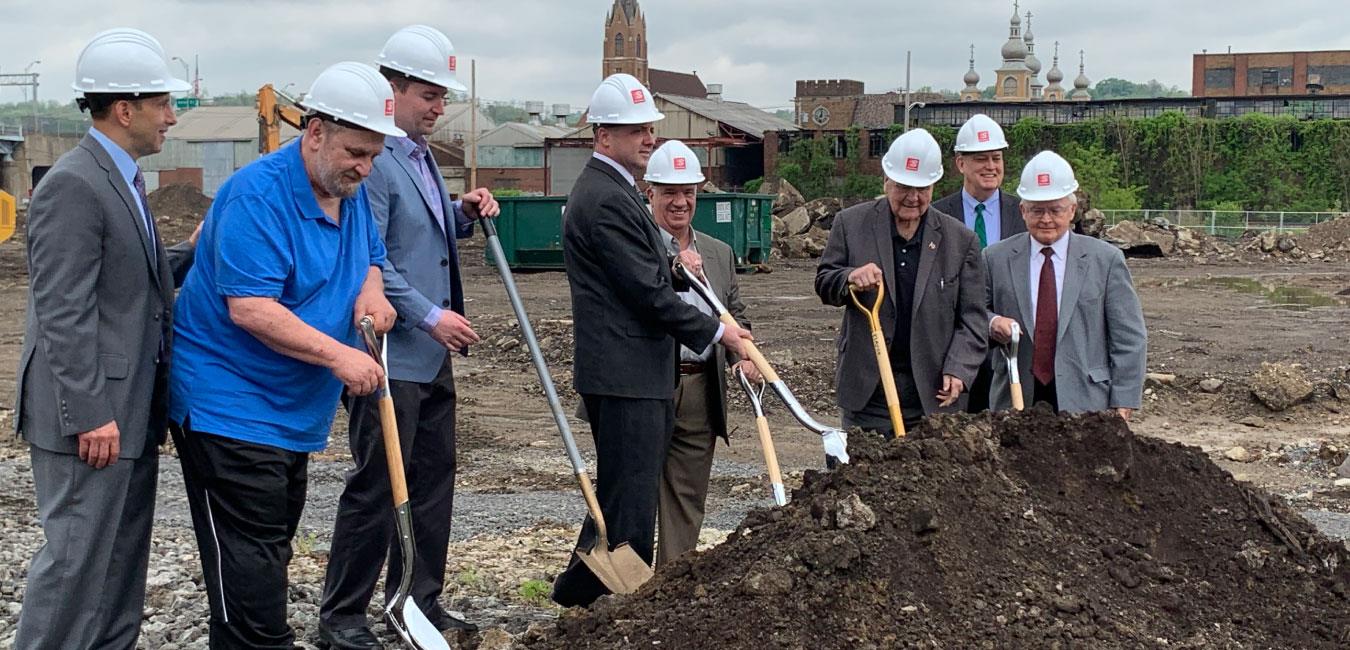 Representative Deasy putting shovel into dirt pile with group of men in hard hats at groundbreaking event